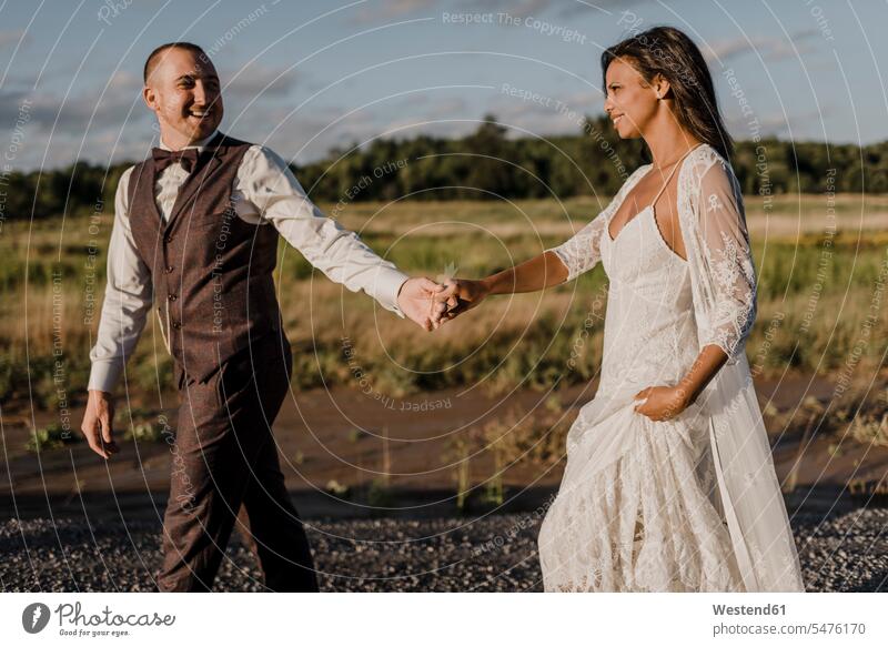 Heterosexual Holding hands and walking against field on sunny day color image colour image outdoors location shots outdoor shot outdoor shots daylight shot