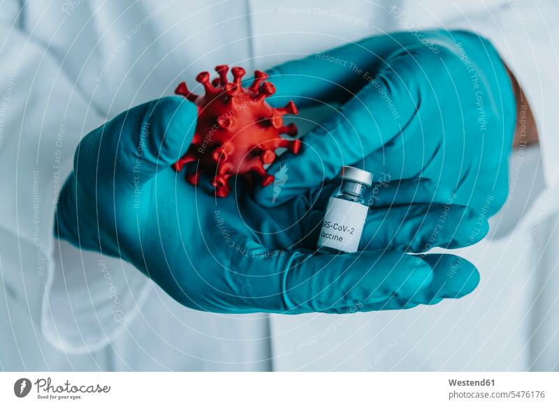 Close-up of scientist hand holding vaccine bottle and coronavirus model while standing at laboratory color image colour image indoors indoor shot indoor shots