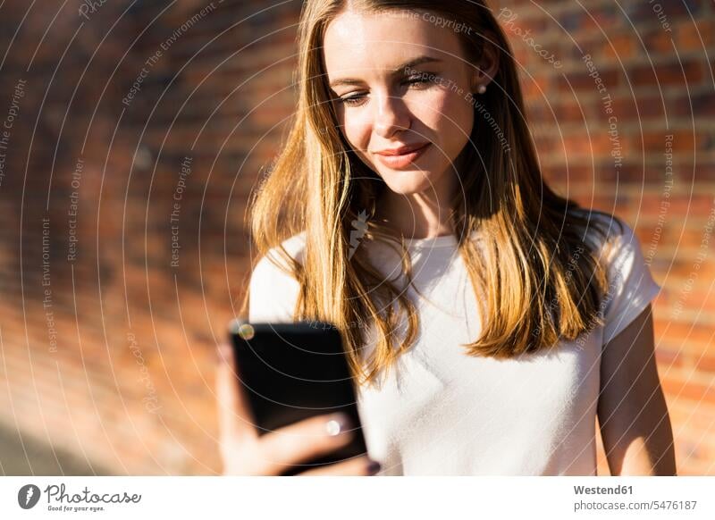 Young woman in front of brick wall, using smartphone happy stand use brick walls telecommunication phones telephone telephones cell phone cell phones Cellphone
