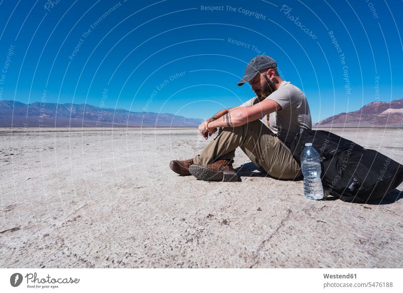 USA, California, Death Valley, man sitting on ground in the desert having a rest men males Seated Deserts break land Adults grown-ups grownups adult people