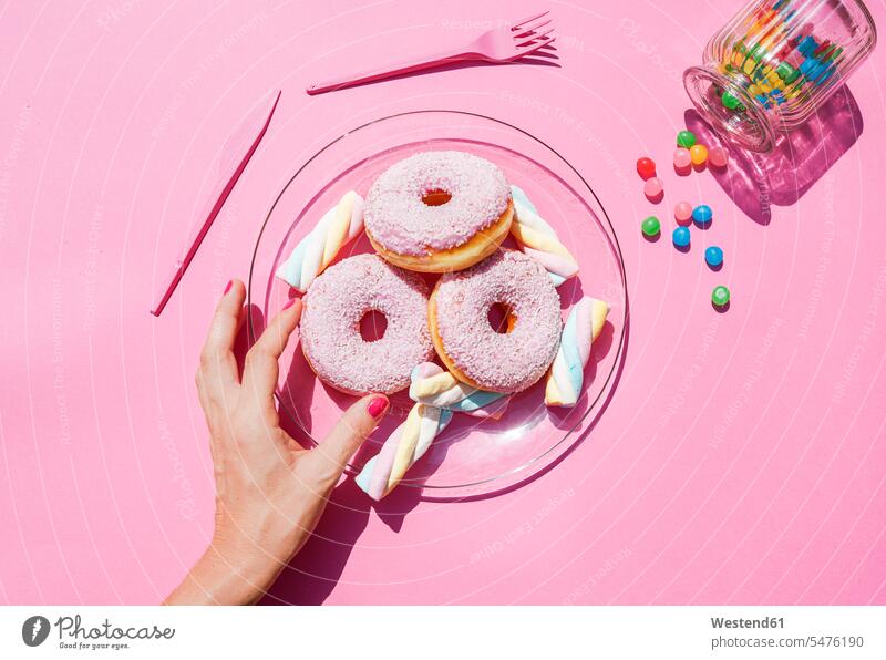 Hand of woman picking up doughnut from plate of sweets overhead view directly above top view studio shot studio photograph studio photographs studio shots