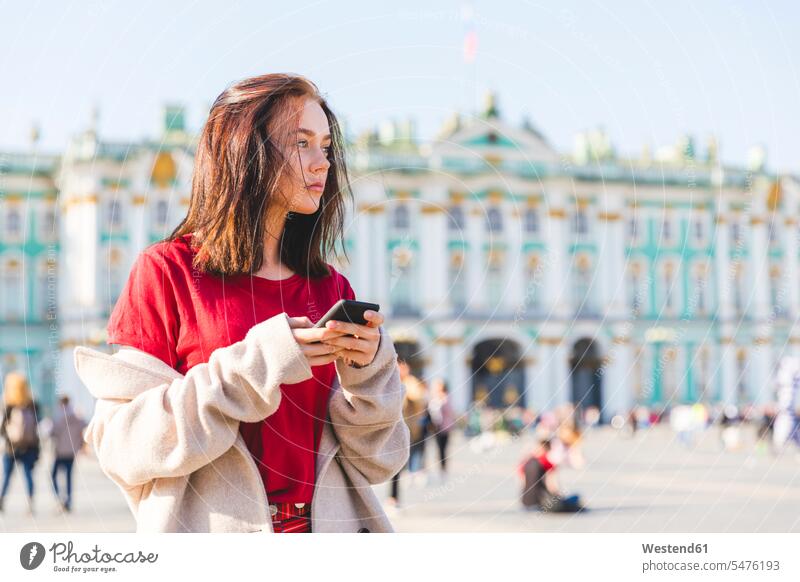 Russia, St. Petersburg, young woman using smartphone in the city looking sideways sideways glance Sideway Glance side glance female tourist mobile phone mobiles
