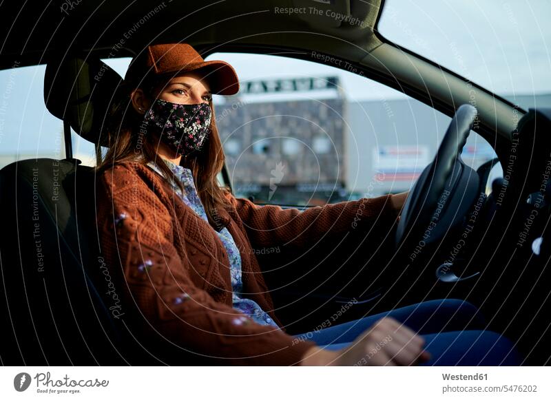 Young woman with cap and face mask driving car in city color image colour image day daylight shot daylight shots day shots daytime casual clothing casual wear