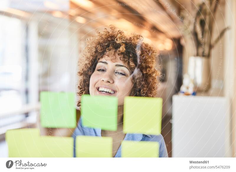 Happy businesswoman brainstorming with post-its on glass pane smiling smile Adhesive Note post-it note sticky notes adhesive notes Brainstorming happiness happy