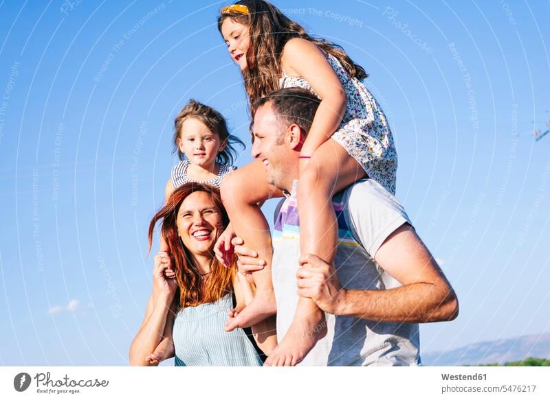 Cheerful parents carrying daughters on shoulders against clear sky during sunny day color image colour image Spain leisure activity leisure activities free time