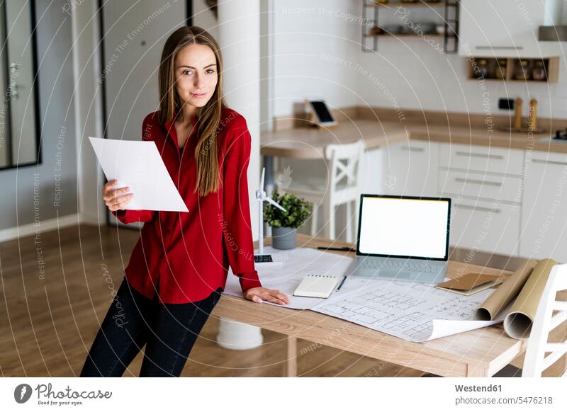 Portrait of smiling woman in office holding paper with wind turbine model on table human human being human beings humans person persons caucasian appearance