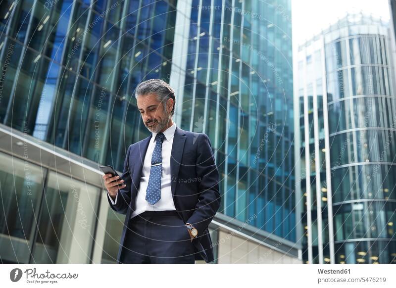 Businessman using mobile phone outside office building in city color image colour image outdoors location shots outdoor shot outdoor shots day daylight shot