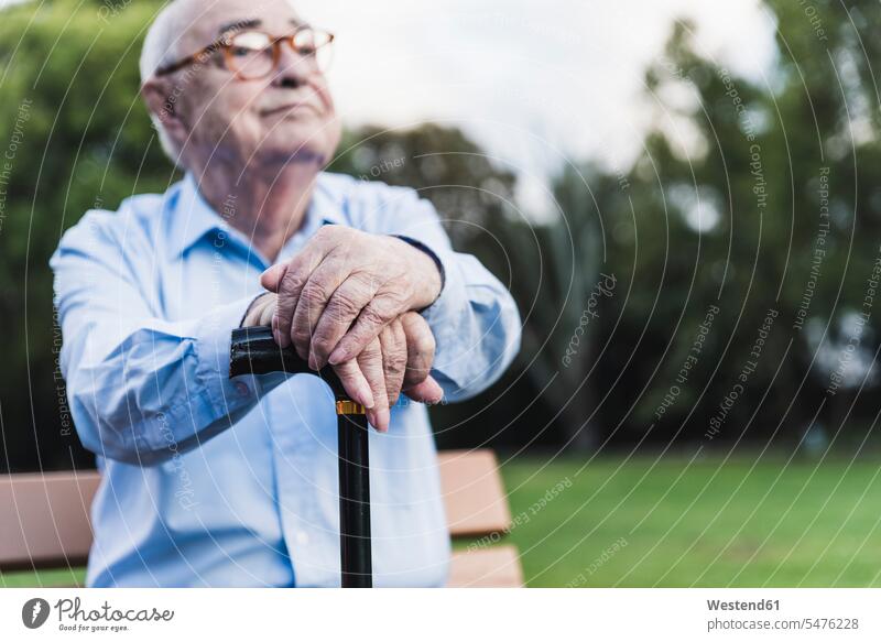 Hands of senior man leaning on walking stick, close-up shirts benches park benches Eye Glasses Eyeglasses specs spectacles Seated sit contemplative Reflective