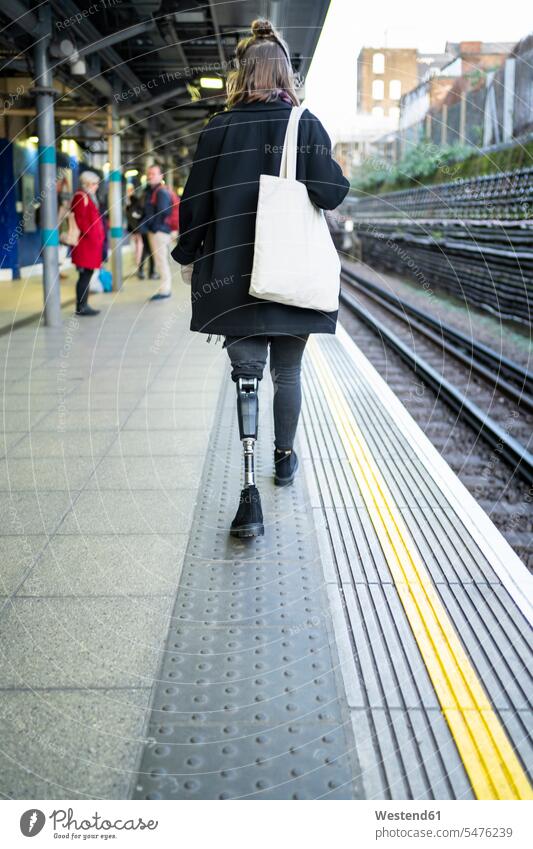 Rear view of young woman with leg prosthesis walking at station platfom human human being human beings humans person persons caucasian appearance