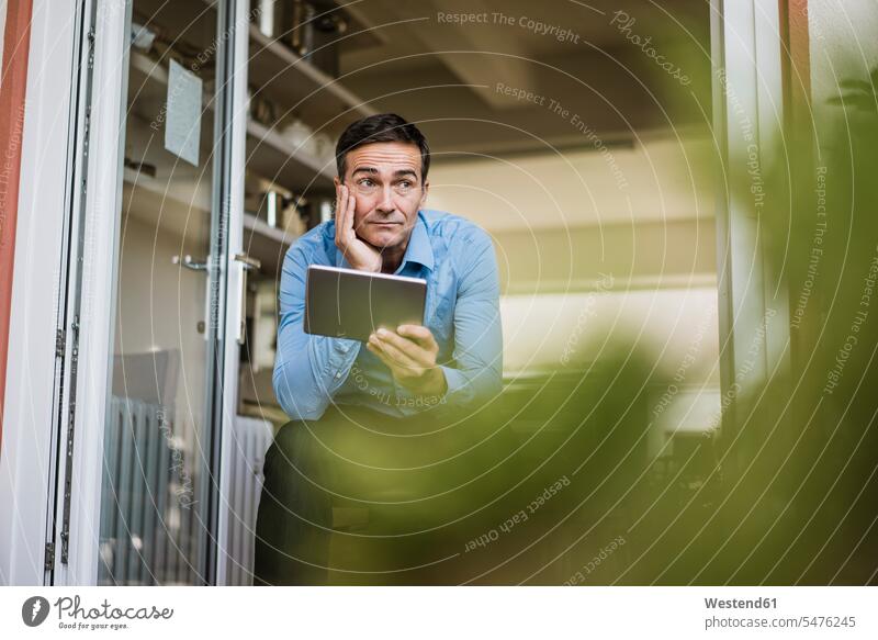 Businessman with tablet sitting at open French door Business man Businessmen Business men French Door opened Seated digitizer Tablet Computer Tablet PC