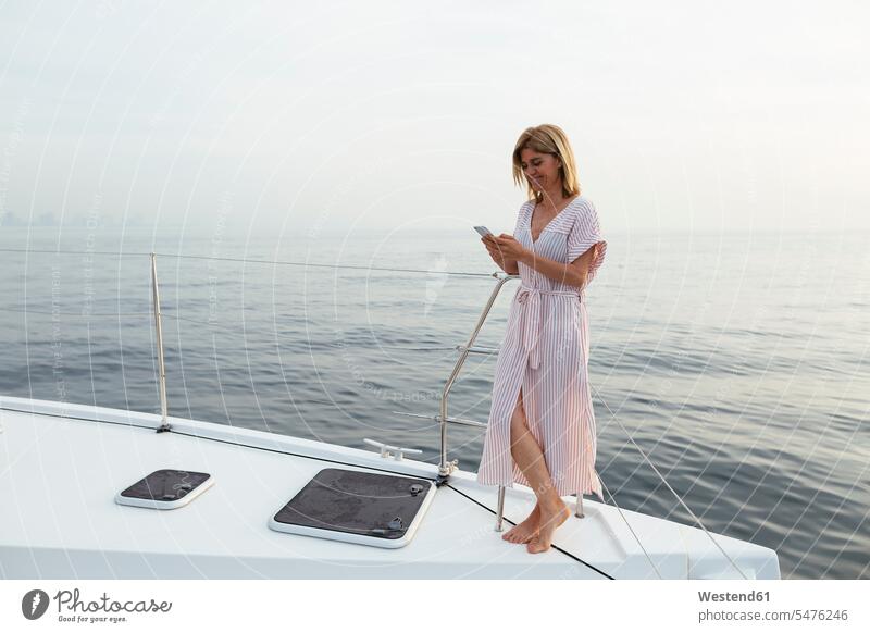 Mature woman standing on catamaran, using smartphone Smartphone iPhone Smartphones mature woman mature women text messaging SMS Text Message reading