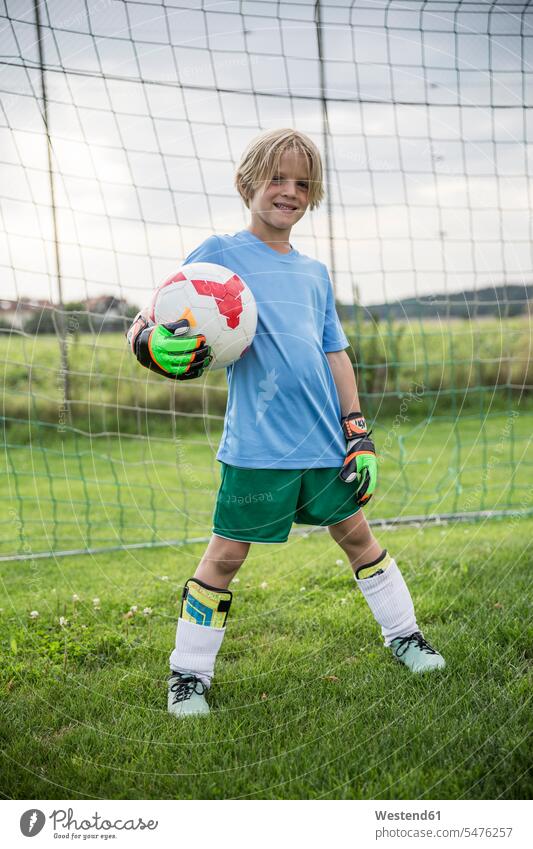 Portrait of smiling young football goalkeeper holding ball on football ground Goalies goalkeepers smile portrait portraits balls soccer soccer pitch