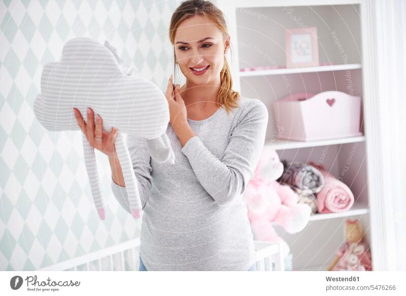 Pregnant woman with cushion and smartphone in baby room Anticipation Expectations Anticipating Anticipate hopeful expectation cushions baby's room Smartphone