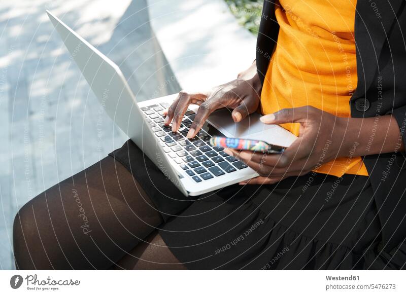 Businesswoman with mobile phone working on laptop color image colour image outdoors location shots outdoor shot outdoor shots day daylight shot daylight shots