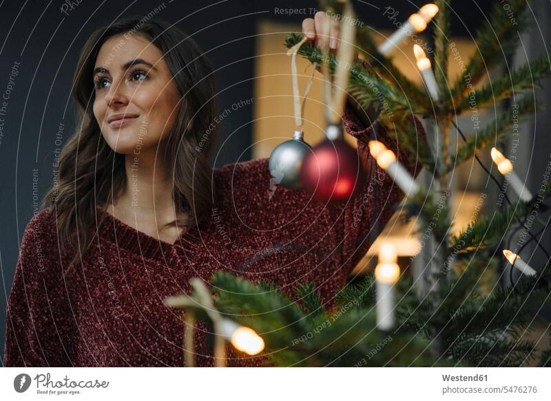 Young woman decorating Christmas tree looking away Germany thinking christmas bauble Christmas tree ball Christmas Ball Bauble christmas baubles