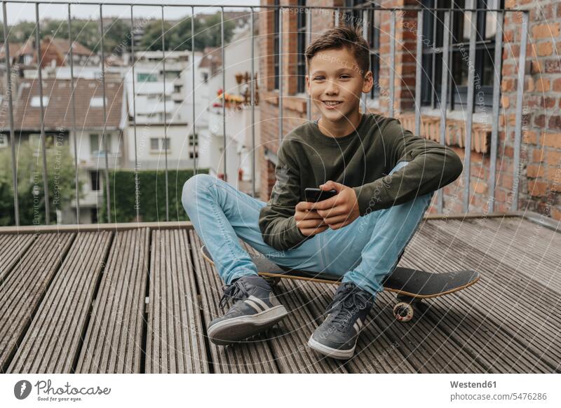 Smiling boy using smart phone while sitting on skateboard against railing color image colour image Germany leisure activity leisure activities free time