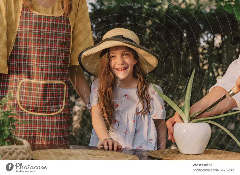 Smiling girl wearing hat standing with mother and grandmother at table in yard color image colour image Spain leisure activity leisure activities free time