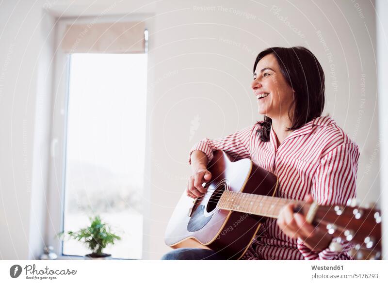 Happy mature woman playing guitar at home brown hair brown haired brown-haired brunette leisure activity leisure activities making music playing music