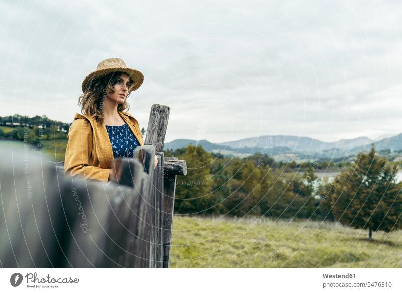 Young curly haired woman wearing a hat, yellow coat and blue t-shirt looking the mountain landscape human human being human beings humans person persons