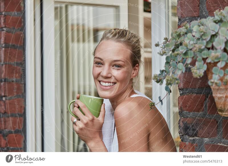 Portrait of smiling sporty young woman with cup of coffee at house entrance Coffee Cup Coffee Cups sportive sporting athletic portrait portraits smile females