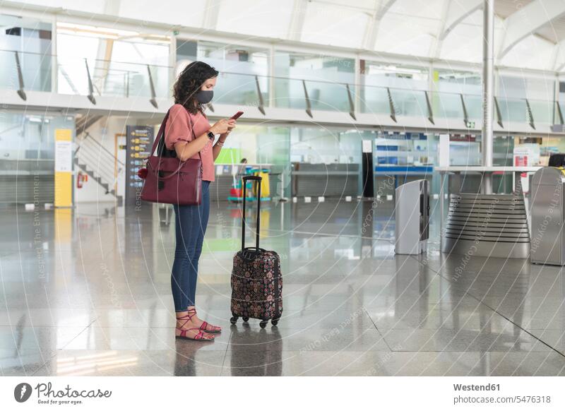 Young woman with protective face mask text messaging on smart phone while standing at airport color image colour image indoors indoor shot indoor shots interior