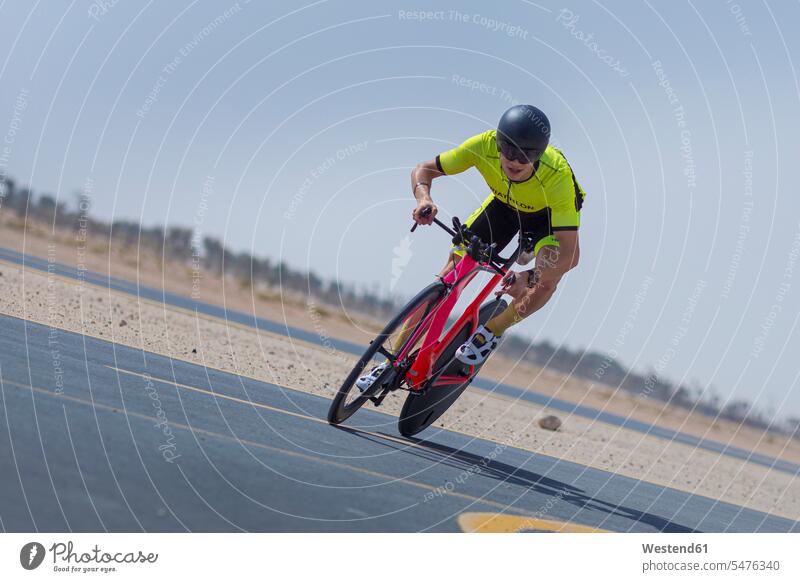 Determined cyclist riding bicycle on road against clear blue sky at desert in Dubai, United Arab Emirates color image colour image outdoors location shots