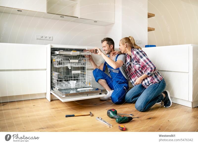 Couple fitting dishwasher in their new built-in kitchen fitted kitchen Fitting assembling installing domestic kitchen kitchens Spirit Level Joy enjoyment