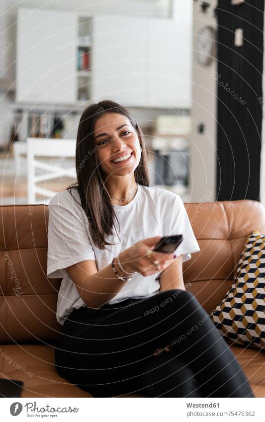 Happy young woman sitting on couch at home watching Tv human human being human beings humans person persons celibate celibates singles solitary people
