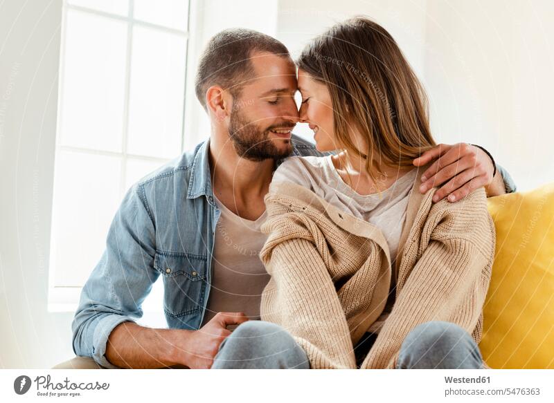 Affectionate smiling couple with closed eyes in love at home windows cushions cuddle snuggle snuggling smile Seated sit embrace Embracement hug hugging relax