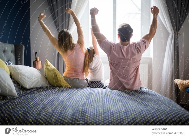 Happy family sitting on bed, stretching, rear view waking up awaking Awakening wake up awake beds families standing up get up getting up stand up Seated people