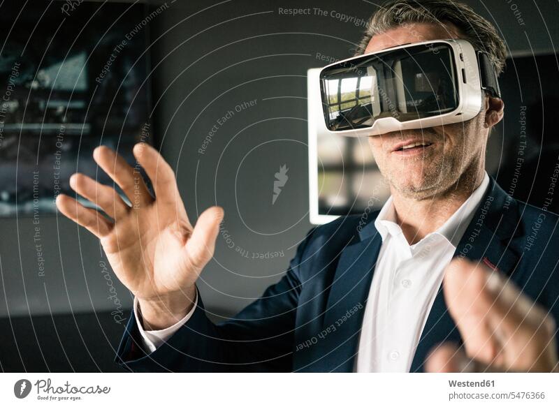 Mature businessman wearing VR glasses in office offices office room office rooms virtual reality specs Eye Glasses spectacles Eyeglasses Businessman