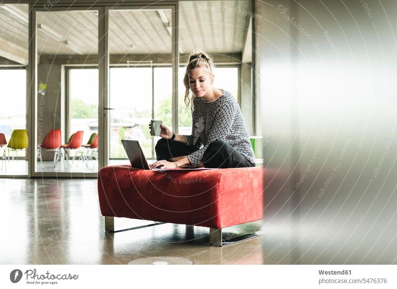 young businesswoman working in modern office, sitting on stool, using laptop Office Offices cross-legged tailor seat businesswomen business woman business women