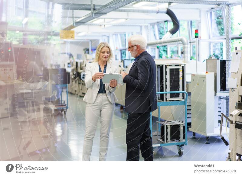 Confident businesswoman discussing over digital tablet with senior businessman in factory color image colour image indoors indoor shot indoor shots interior