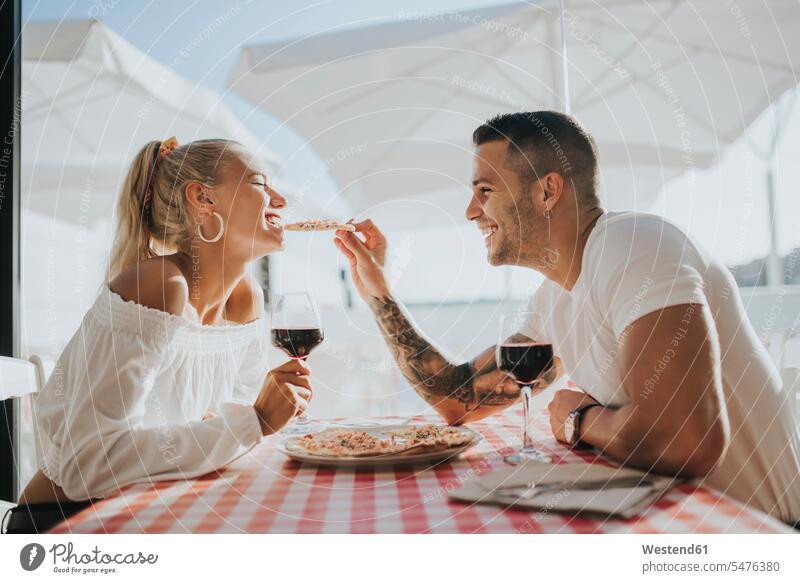 Happy young man feeding pizza to girlfriend while sitting in restaurant color image colour image Spain leisure activity leisure activities free time