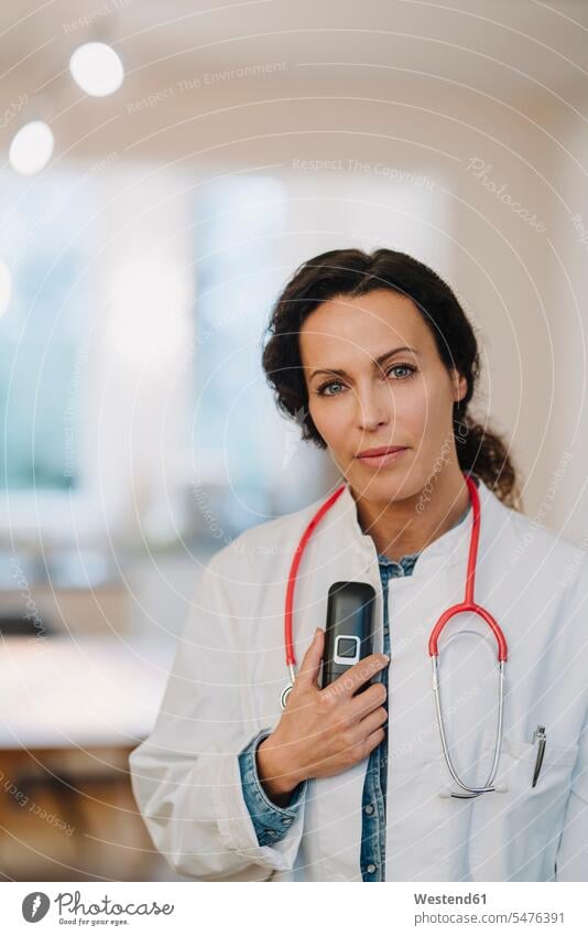 Female doctoe standing in hosptal, holding telephone and stethoscope human human being human beings humans person persons caucasian appearance