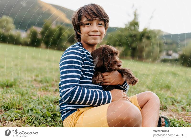Boy holding puppy while sitting on grass at backyard color image colour image outdoors location shots outdoor shot outdoor shots day daylight shot