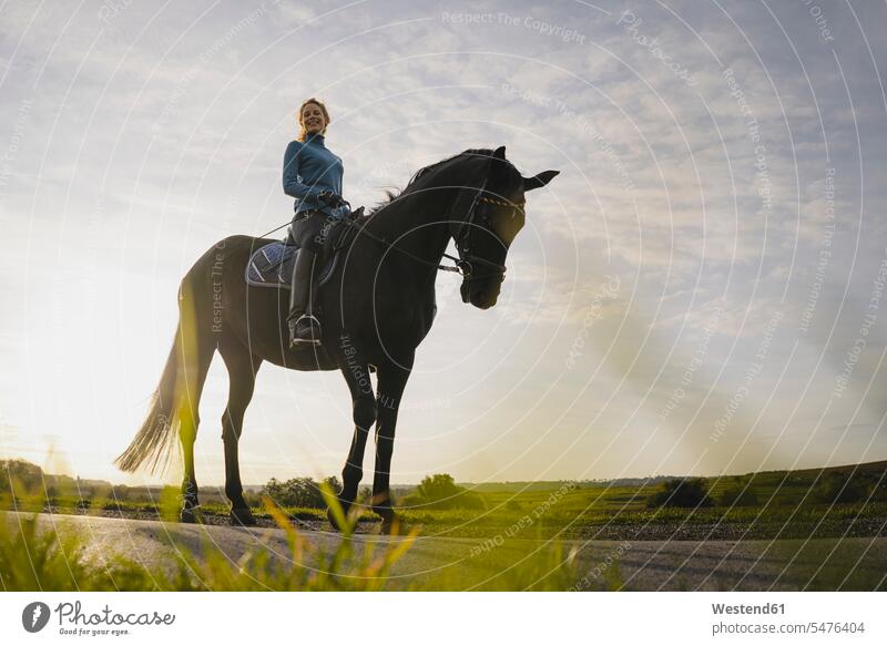 Woman on horse on a road in the countryside smile horse riding ride in the evening Late Evening delight enjoyment Pleasant pleasure indulgence indulging