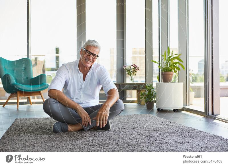 Portrait of smiling mature man relaxing sitting on carpet at home men males portrait portraits relaxed relaxation Seated smile carpets rug rugs Adults grown-ups