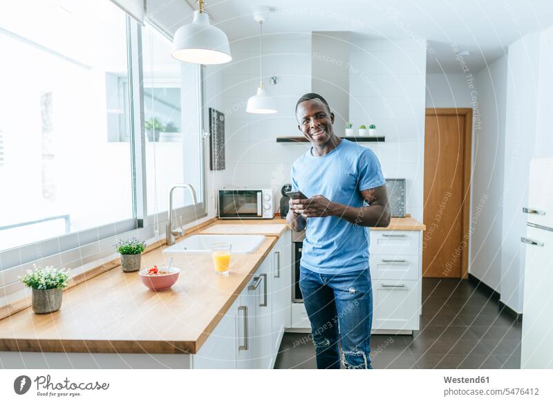 Portrait of happy young man using cell phone in kitchen at home human human being human beings humans person persons African black black ethnicity coloured 1