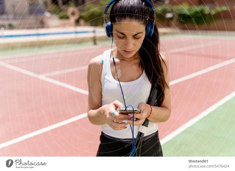 Female tennis player using smart phone while listening music in court on sunny day color image colour image Spain outdoors location shots outdoor shot