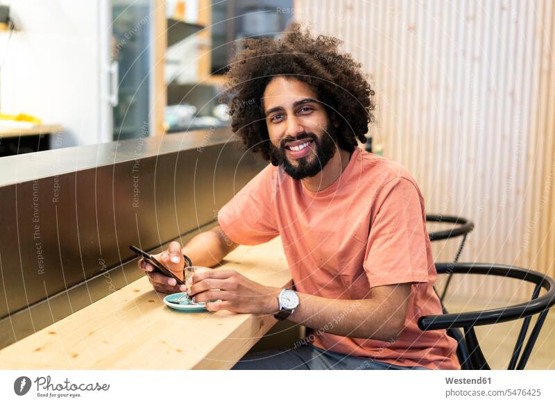 Portrait of a smiling man with cell phone sitting at the counter of a bar human human being human beings humans person persons celibate celibates singles