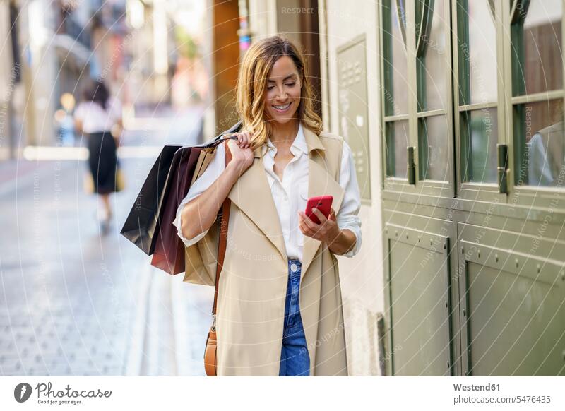 Woman with shopping bag using mobile phone while standing at footpath in city color image colour image outdoors location shots outdoor shot outdoor shots day
