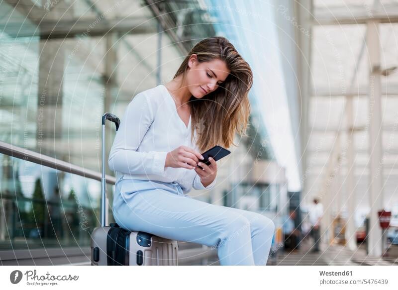 Young businesswoman sitting outdoors on luggage using cell phone suitcase suitcases Seated baggage mobile phone mobiles mobile phones Cellphone cell phones