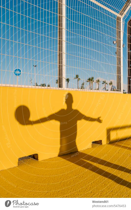 Shadow of young man holding basketball on yellow wall in sports court color image colour image Spain leisure activity leisure activities free time leisure time