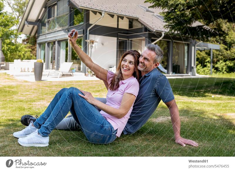 Happy couple sitting in garden of their home taking a selfie happiness happy house houses Selfie Selfies gardens domestic garden twosomes partnership couples