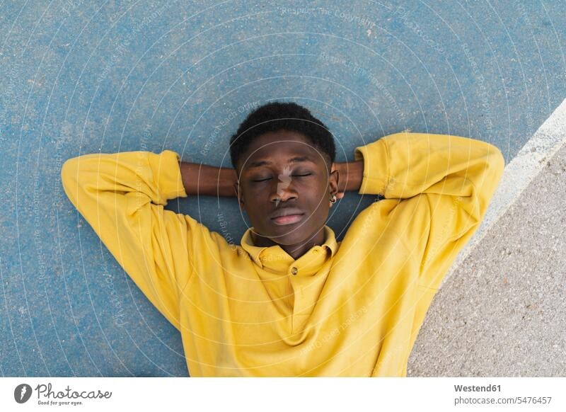 Young black man sleeping on floor, with hands behind head African descent coloured portrait portraits yellow shirt shirts asleep floors lying laying down lie