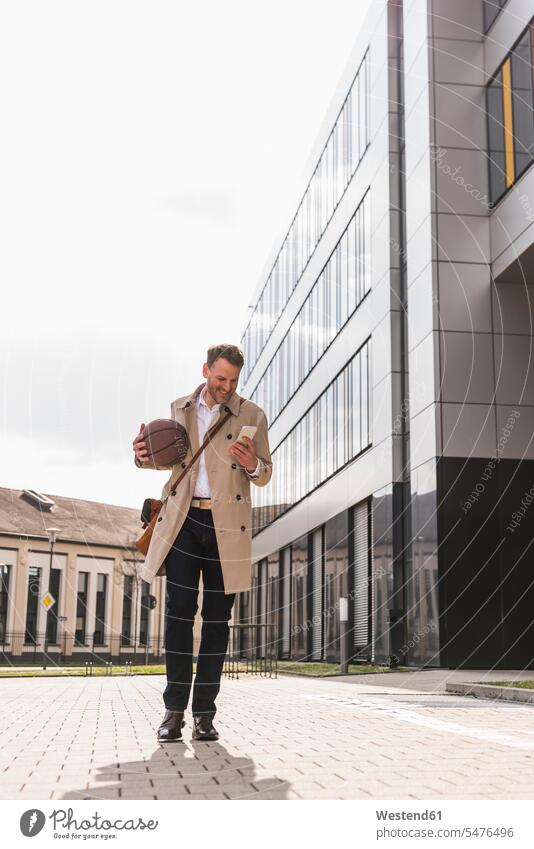 Smiling businessman with cell phone and basketball outside office building office buildings Businessman Business man Businessmen Business men happiness happy