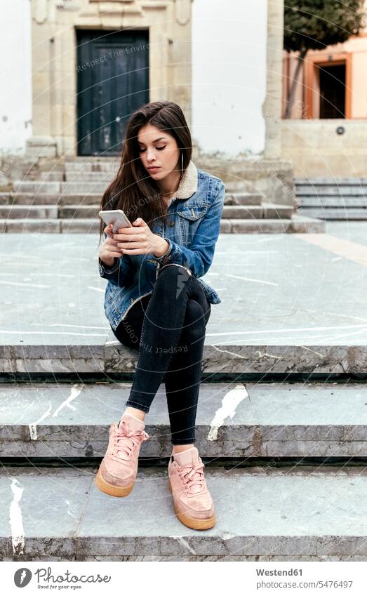 Young woman sitting on stairs in a town checking her smartphone Town Smartphone iPhone Smartphones stairway females women brown hair brown haired brown-haired
