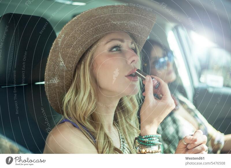 Beautiful woman applying lipstick in car during road trip color image colour image Vehicle Interior day daylight shot daylight shots day shots daytime USA