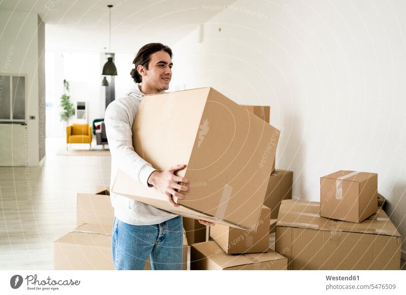 Smiling young man carrying cardboard box while moving in new apartment color image colour image indoors indoor shot indoor shots interior interior view